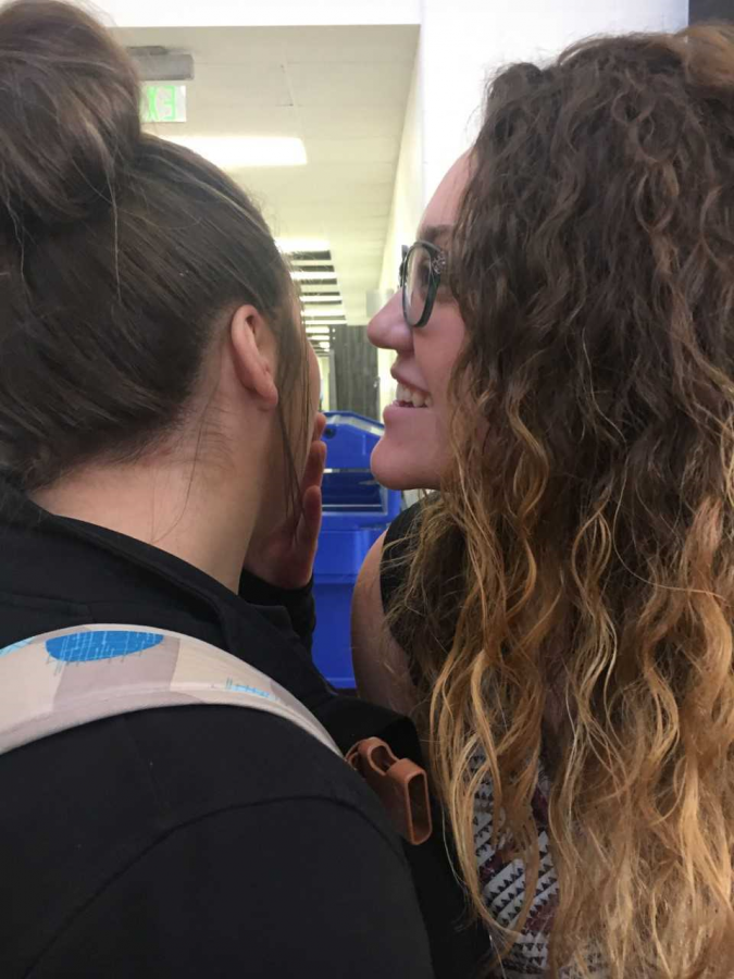 One student whispers a secret into the ear of another.