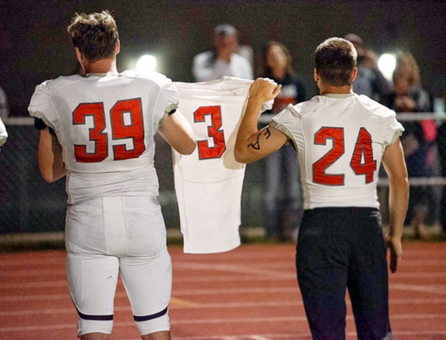 (From left to right) Senior Carson Olsen and junior Kadden Abraham hold teammate Ethan Asher’s No.3 jersey during Friday’s football game in Riverton. 