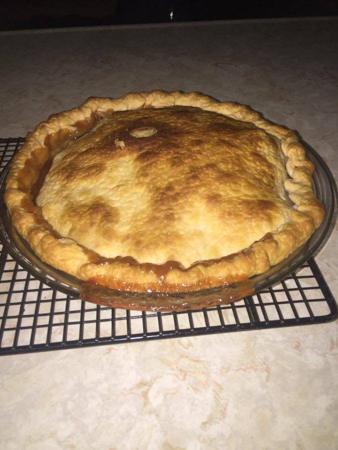 An apple pie sits, cooling on a rack, after being taken out of the oven. 
