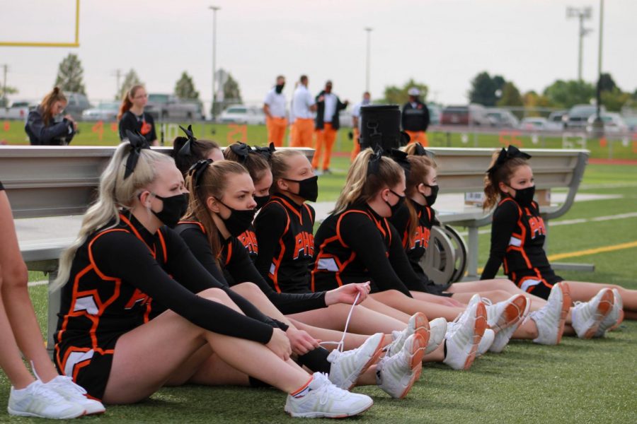 The Powell High School Cheerleading Team wears their masks while sitting on the sidelines.  