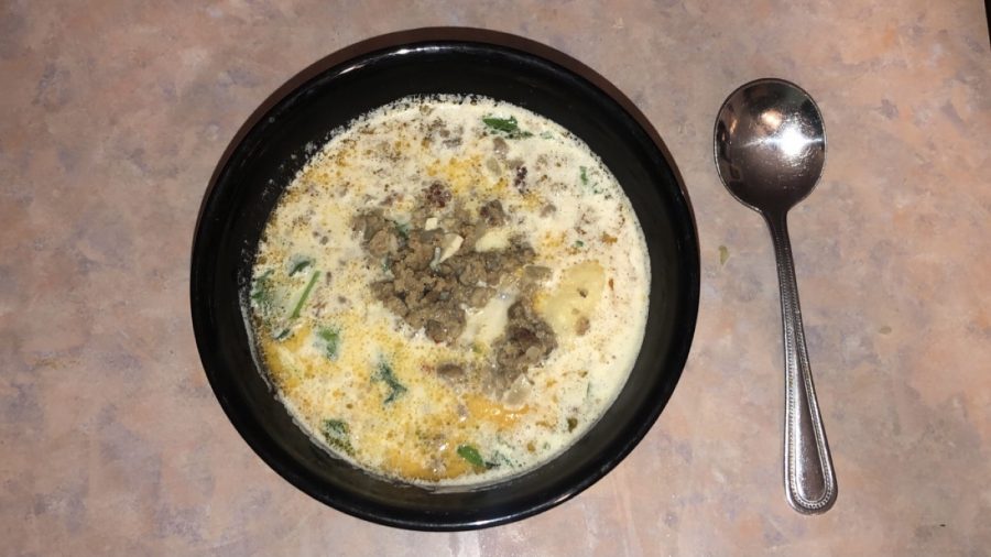 Presented is a bowl of Zuppa Toscana topped with fresh cream and kale. 