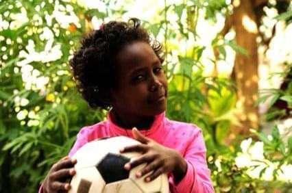 Junior Bereket Burns holds a soccer ball as a young child while in her homeland, Ethiopia.