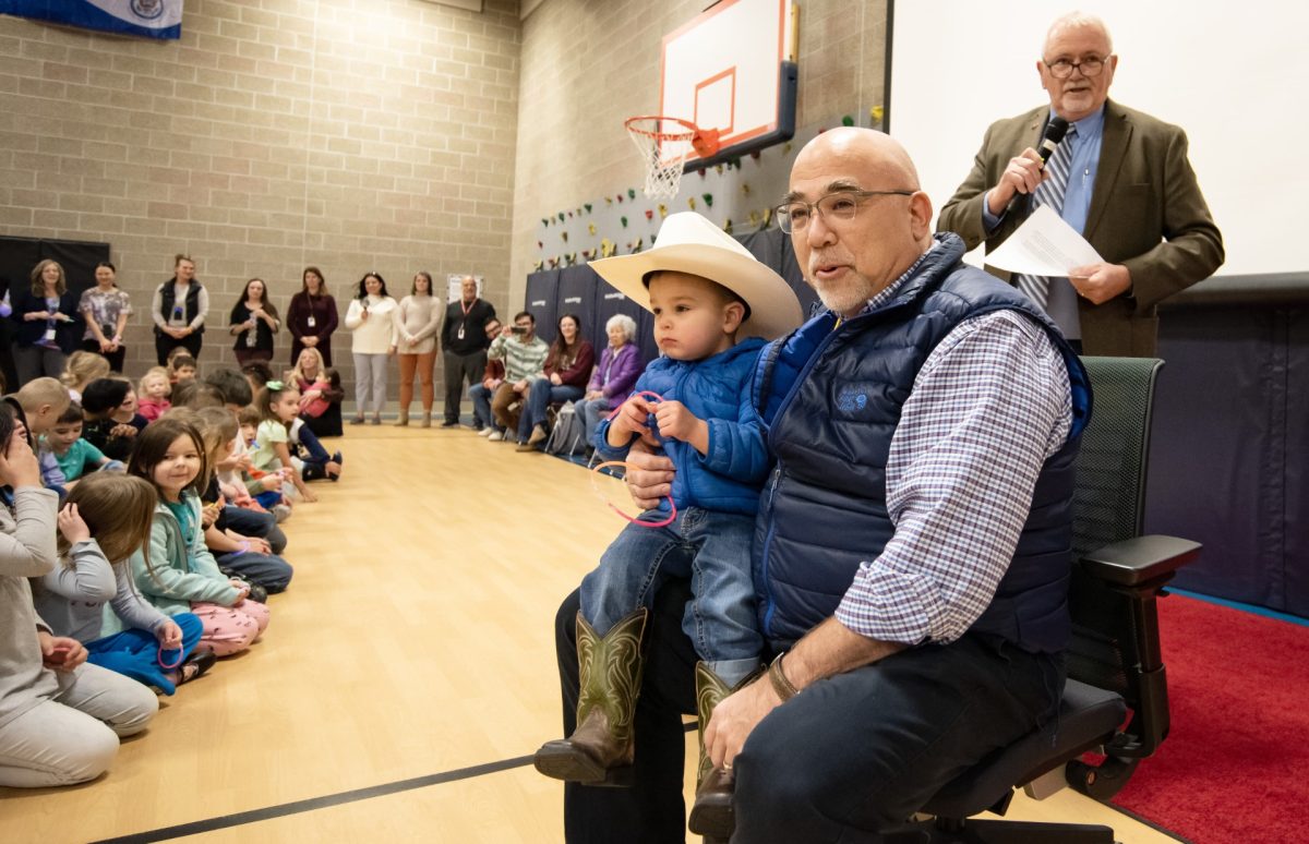 At the Southside assembly, Mr. Scott Schiller sits in front of the crowd. In his lap is his grandson, Atticus James Schiller, and behind is Kenny Jones, a former principal at Parkside Elementary, and currently the Executive Director of the Wyoming Association of Elementary and Middle School Principals. Photo courtesy of Mark Davis, of the Powell Tribune.
