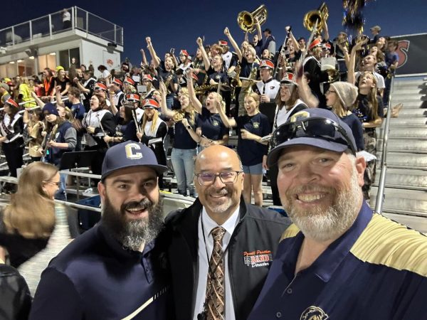 Band directors pose for a picture while their musicians cheer.