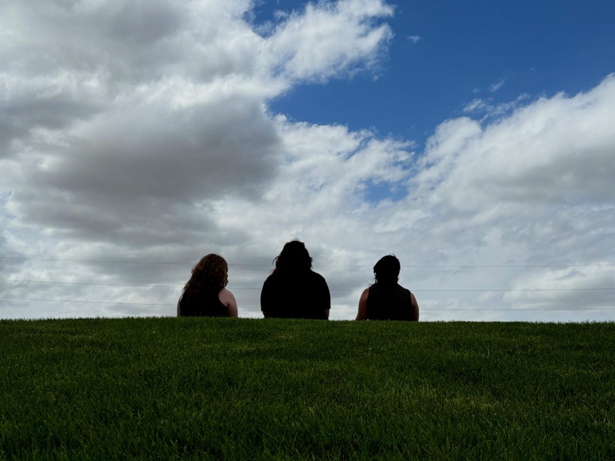 Ashton McDaniel, Deeanna Gibson, and Casey Thormahlen sit on a hill outside Powell High School and ponder. 