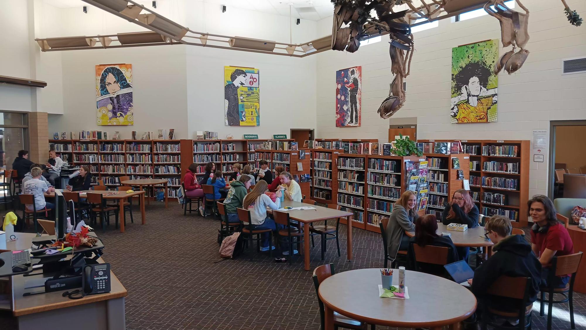 Students collaborate at different tables during their lunch in the library.