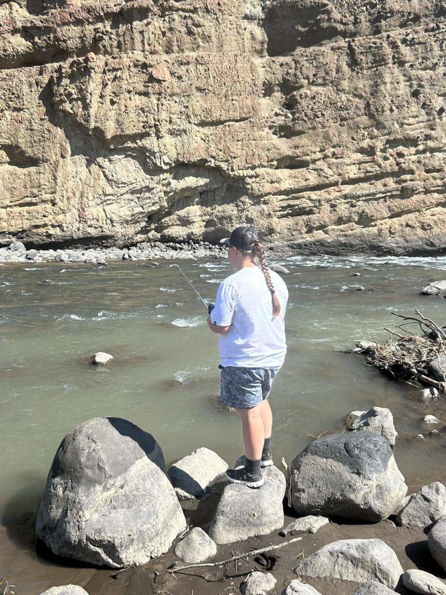 Gabi stands out on a rock in the river as she fishes.
